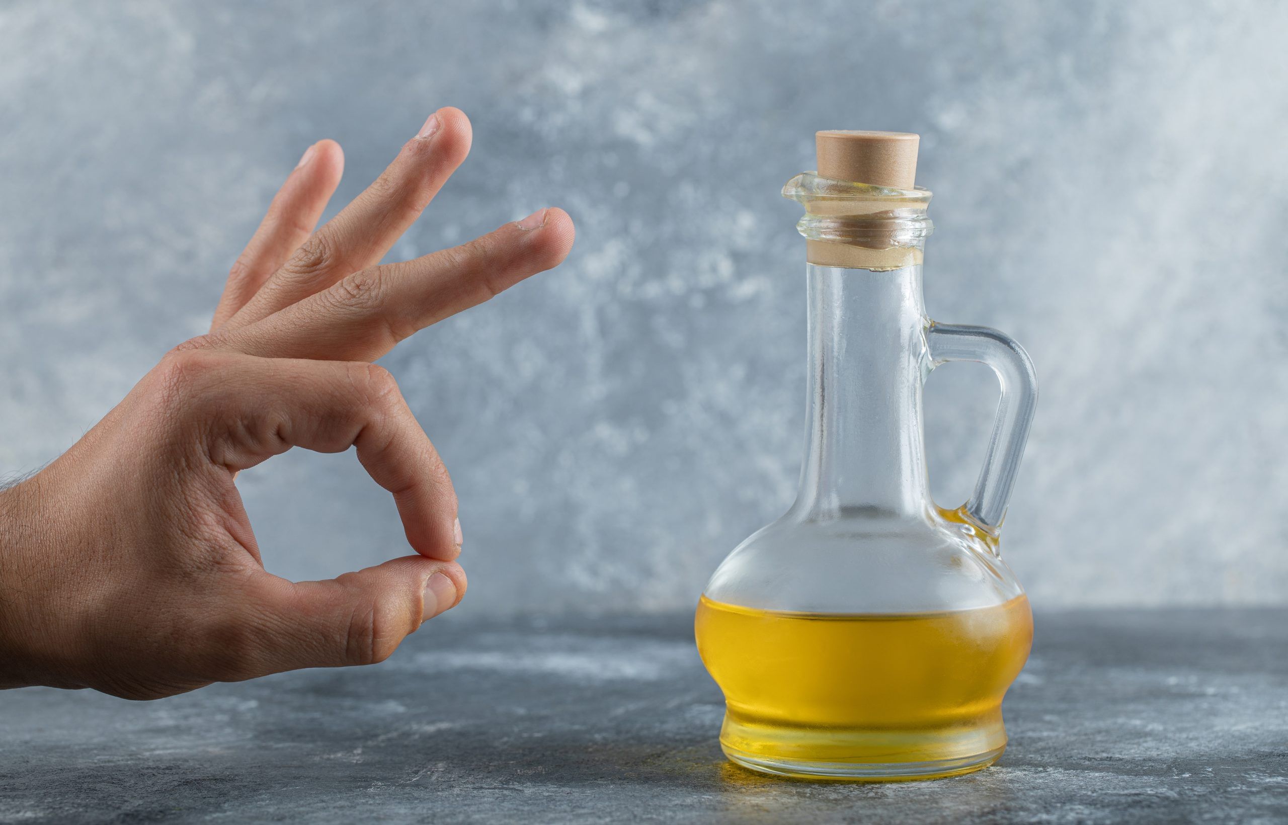 Man gesturing ok with hand behind of bottle of oil