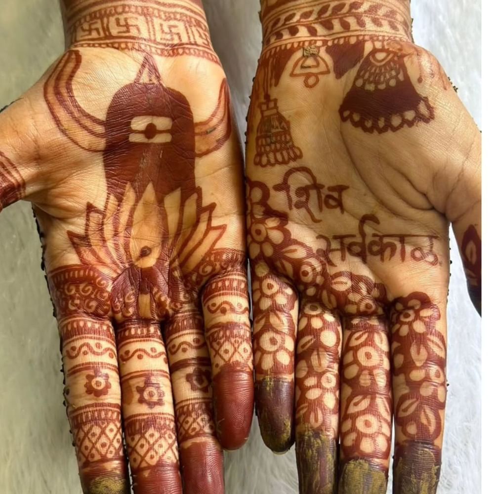 ਇਹ ਮਹਿੰਦੀ ਡਿਜ਼ਾਈਨ ਵੀ ਬਹੁਤ ਸੁੰਦਰ ਲੱਗ ਰਿਹਾ ਹੈ। ਇਸ ਵਿੱਚ ਇੱਕ ਪਾਸੇ ਕਮਲ ਦਾ ਫੁੱਲ, ਸ਼ਿਵਲਿੰਗ ਅਤੇ ਤ੍ਰਿਸ਼ੂਲ ਬਣਾਏ ਗਏ ਹਨ। ਸਵਾਸਤਿਕ ਵੀ ਬਣਾਇਆ ਗਿਆ ਹੈ। ਤੁਸੀਂ ਇਸ ਮਹਿੰਦੀ ਡਿਜ਼ਾਈਨ ਤੋਂ ਵੀ ਆਈਡੀਆ ਲੈ ਸਕਦੇ ਹੋ। ਜੇਕਰ ਤੁਸੀਂ ਮਹਿੰਦੀ ਲਗਾਉਣੀ ਜਾਣਦੇ ਹੋ ਤਾਂ ਇਸ ਡਿਜ਼ਾਈਨ ਨੂੰ ਘਰ 'ਤੇ ਲਗਾਉਣਾ ਬਹੁਤ ਆਸਾਨ ਹੋ ਜਾਵੇਗਾ। ( Credit : nails_and_stains )