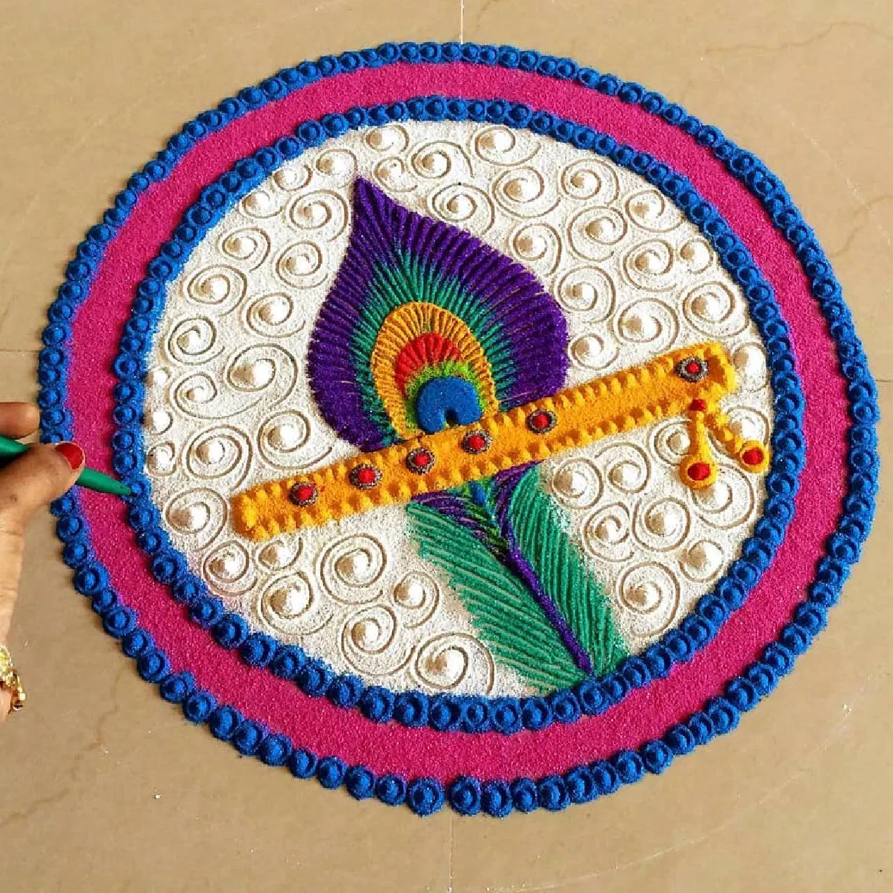 ਰੰਗੋਲੀ ਦਾ ਇਹ ਡਿਜ਼ਾਈਨ ਬਹੁਤ ਸੁੰਦਰ ਦਿਖਾਈ ਲੱਗ ਰਿਹਾ ਹੈ। ਇਸ ਵਿੱਚ ਗੋਲਾ ਬਣਾ ਕੇ ਅੰਦਰ ਨੀਲਾ, ਚਿੱਟਾ ਅਤੇ ਜਾਮਨੀ ਰੰਗ ਭਰਿਆ ਗਿਆ ਹੈ। ਨਾਲ ਹੀ, ਬੰਸਰੀ ਅਤੇ ਮੋਰ ਦੇ ਪੰਖ ਦਾ ਡਿਜ਼ਾਈਨ ਬਣਾਇਆ ਗਿਆ ਹੈ। ਇਸਨੂੰ ਬਣਾਉਣਾ ਵੀ ਆਸਾਨ ਹੋਵੇਗਾ। ਤੁਸੀਂ ਘਰ ਵਿੱਚ ਇਸ ਡਿਜ਼ਾਈਨ ਦੀ ਰੰਗੋਲੀ ਵੀ ਬਣਾ ਸਕਦੇ ਹੋ। (Credit : fun_with_rangoli )