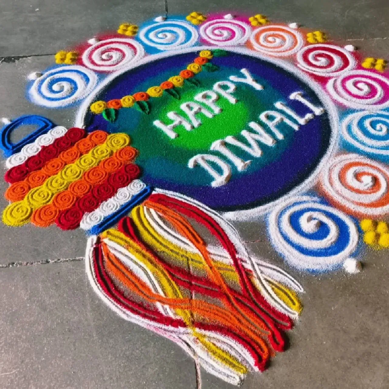 ਦੀਵਾਲੀ ਲਈ ਤੁਸੀਂ ਇਹ ਰੰਗੋਲੀ ਡਿਜ਼ਾਈਨ ਵੀ ਅਜ਼ਮਾ ਸਕਦੇ ਹੋ। ਇਸ ਵਿੱਚ ਹਰੇ ਅਤੇ ਨੀਲੇ ਰੰਗਾਂ ਨਾਲ ਗੋਲ ਘੇਰਾ ਬਣਾਕੇ ਅੰਦਰ “Happy Diwali” ਲਿਖਿਆ ਗਿਆ ਹੈ। ਬਾਹਰੀ ਹਿੱਸੇ ਵਿੱਚ ਛੋਟੇ-ਛੋਟੇ ਸਰਕਲ ਅਤੇ ਇੱਕ ਪਾਸੇ ਝਾਲਰ (ਝੂਮਰ) ਦਾ ਡਿਜ਼ਾਈਨ ਬਣਾਇਆ ਗਿਆ ਹੈ। ਨਾਲ ਹੀ ਰੰਗਾਂ ਨਾਲ ਫੁੱਲ ਅਤੇ ਪੱਤਿਆਂ ਦੀ ਤੋਰਨ ਵੀ ਸਜਾਈ ਗਈ ਹੈ।
