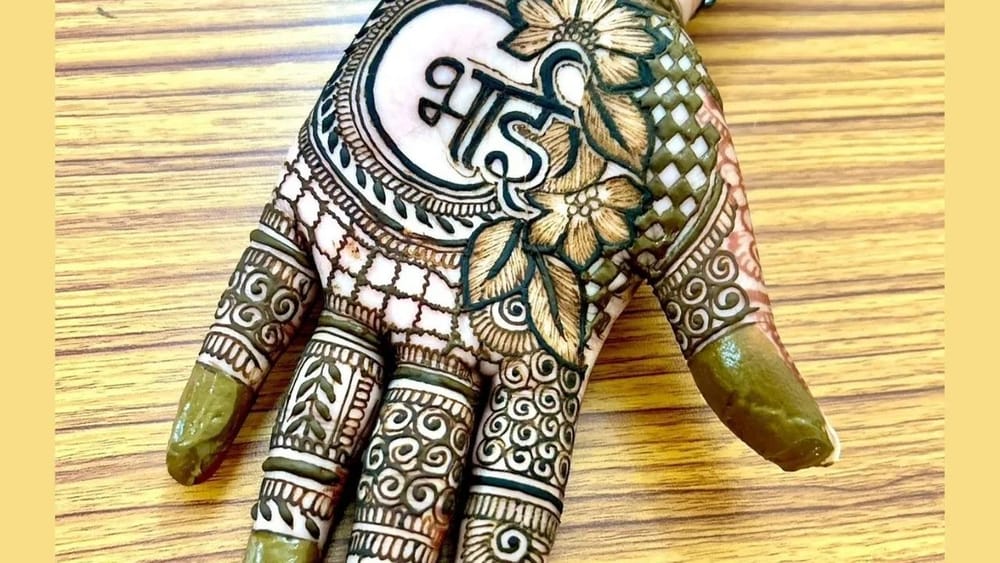 ਇਹ ਮਹਿੰਦੀ ਡਿਜ਼ਾਈਨ ਸਿੰਪਲ ਅਤੇ ਸੋਬਰ ਹੋਣ ਦੇ ਨਾਲ-ਨਾਲ ਝੱਟਪੱਟ ਵੀ ਲੱਗ ਜਾਵੇਗੀ     ਅਤੇ ਰਚਣ ਤੋਂ ਬਾਅਦ ਬੇਹੱਦ ਖੂਬਸੂਰਤ ਲੱਗੇਗਾ। ਸਭ ਤੋਂ ਪਹਿਲਾਂ ਤੁਹਾਨੂੰ ਹਥੇਲੀ ਦੇ ਉੱਪਰਲੇ ਹਿੱਸੇ ਵਿੱਚ ਫੁੱਲ ਬਣਾਕੇ ਡਿਜ਼ਾਈਨ ਪੂਰਾ ਕਰਨਾ ਹੈ। ਇਸ ਤੋਂ ਬਾਅਦ ਹਾਫ ਕਰਵ ਬਣਾਕੇ ‘ਰੱਖੜੀ’ ਲਿਖੋ। ਹੁਣ ਇਸ ਦੇ ਉੱਪਰ ਡਬਲ ਆਊਟਲਾਈਨ ਅਤੇ ਹੰਪ ਦੀਆਂ ਦੋ ਲਾਈਨਾਂ ਬਣਾਓ। ਕਰਵ ਬਣਾਕੇ ਫਿਲ ਕਰੋ ਅਤੇ ਫਿਰ ਡ੍ਰਾਪ ਚੇਨ ਬਣਾ ਦਿਓ। ਹੁਣ ਉਂਗਲਾਂ ਅਤੇ ਅੰਗੂਠੇ ਦੀ ਮਹਿੰਦੀ ਦਾ ਡਿਜ਼ਾਈਨ ਪੂਰਾ ਕਰ ਲਓ। (Image: zeenat_mehandi_desingn)